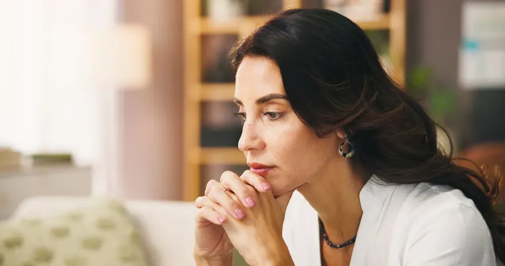 A woman lost in thought, hands clasped under her chin